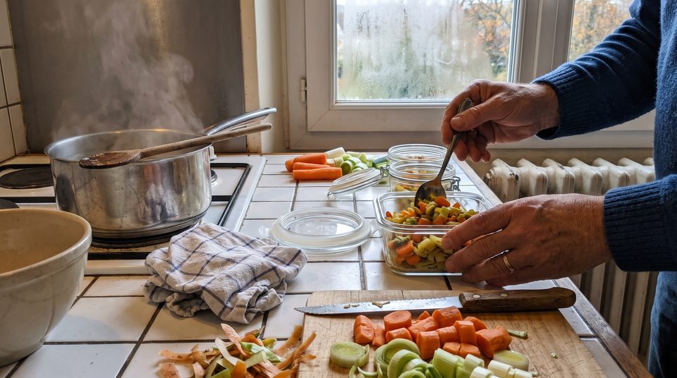 Plan de travail en plein batch cooking : boîtes en verre, légumes coupés et casserole qui mijote