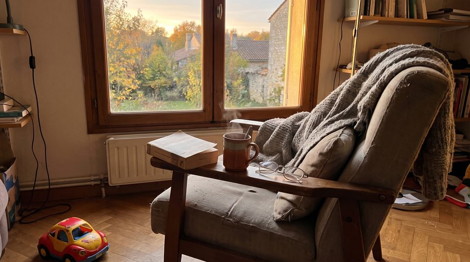 Tasse de thé et livre ouvert sur l'accoudoir d'un fauteuil près d'une fenêtre, plaid en laine